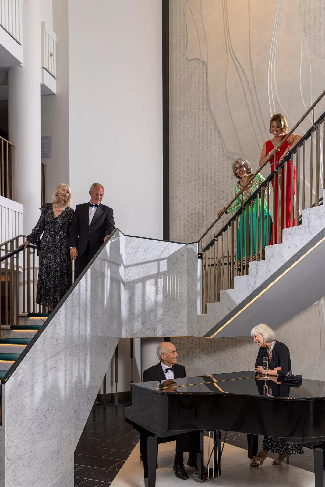 Saga cruise atrium photography — guests in evening wear on the grand staircase with a pianist at the marble foot