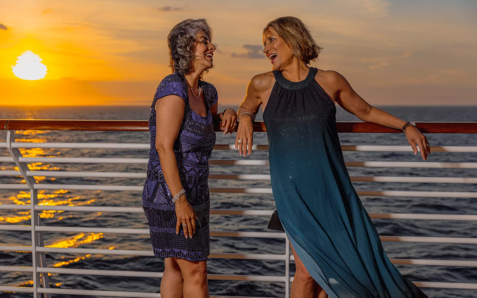 Saga cruise lifestyle photography — two women laughing on deck at sunset, sea behind