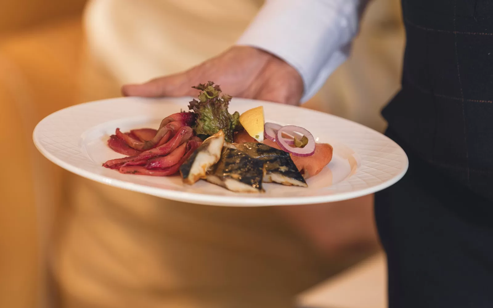 Saga cruise fine-dining photography — plated fish course of mackerel and smoked salmon held by a waiter