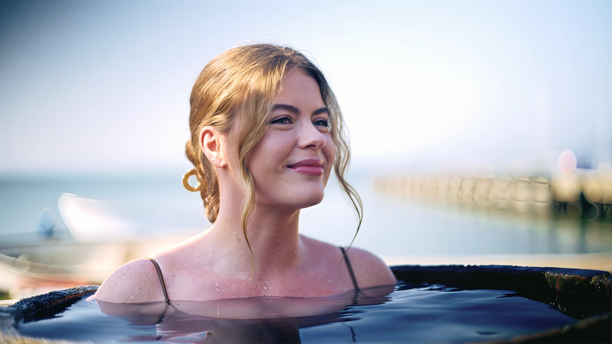 Visit Kent tourism photography — woman relaxing in an outdoor bath with the Kent coast and pier behind